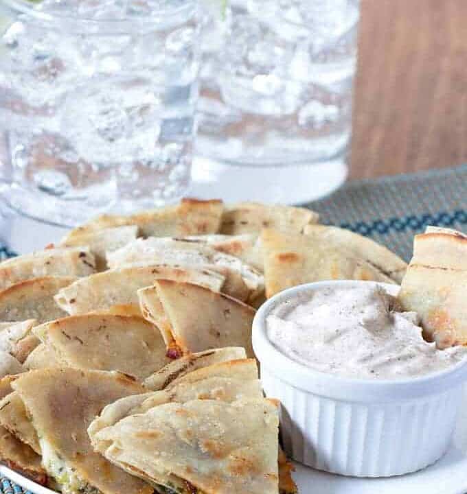 Small quesadillas cut into triangles on a plate with a side of creamy dip.