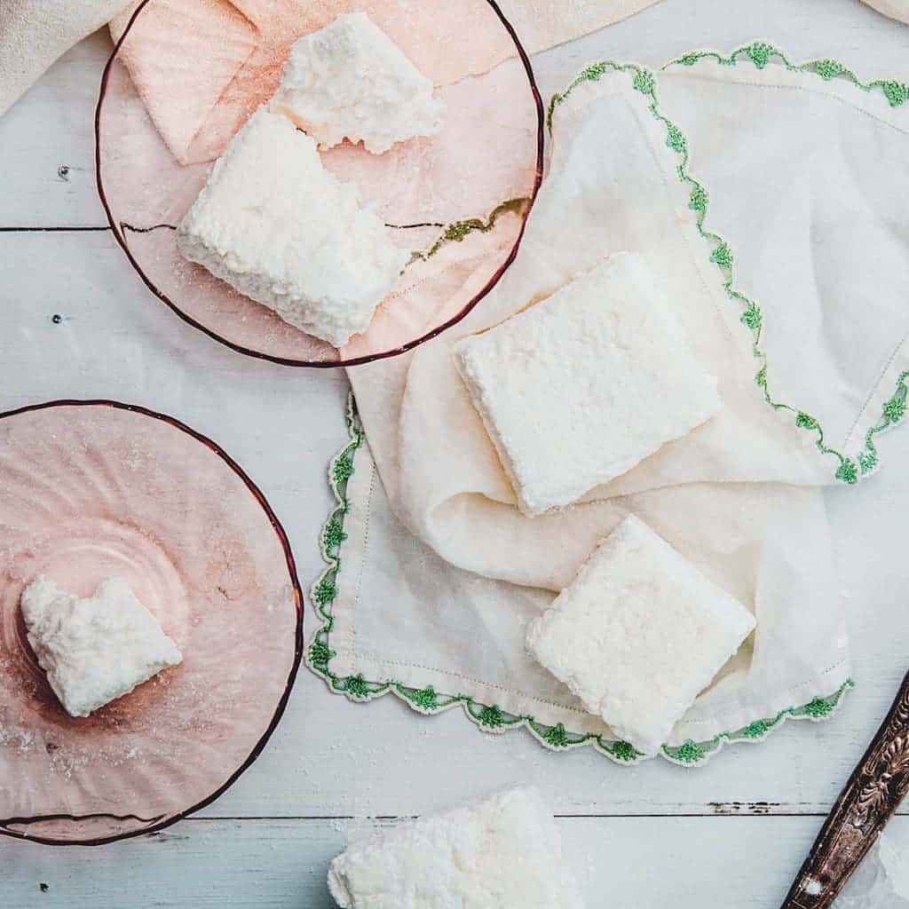 Two marshmallows on a white and green handkerchief next to two partially eaten marshmallows on pink plates.