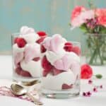 Two glass cups filled with whipped mascarpone cream and heart meringue cookies with flowers in the background.