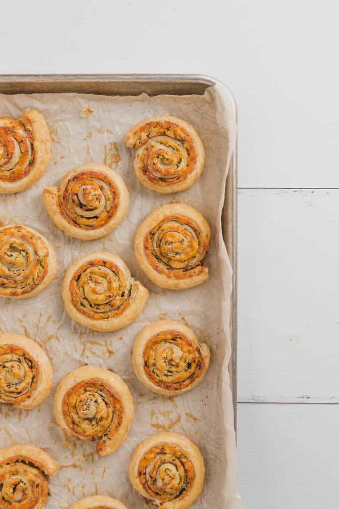 Overhead view of a sheet pan with parchment and baked white cheddar prosciutto pinwheels
