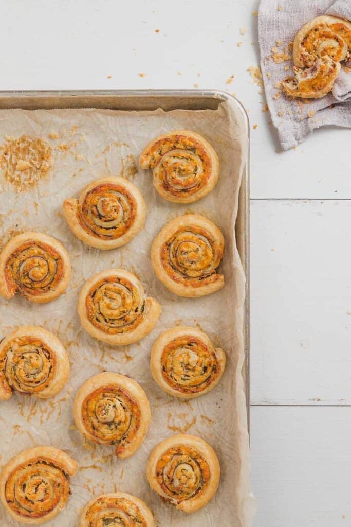 overhead of white cheddar prosciutto pinwheels on a baking sheet with broken pinwheel in corner