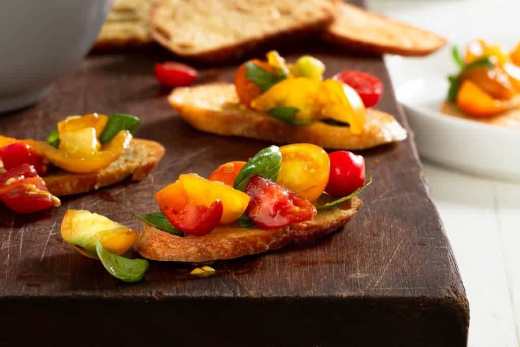 pieces of crostini topped with bruschetta on a wood board.