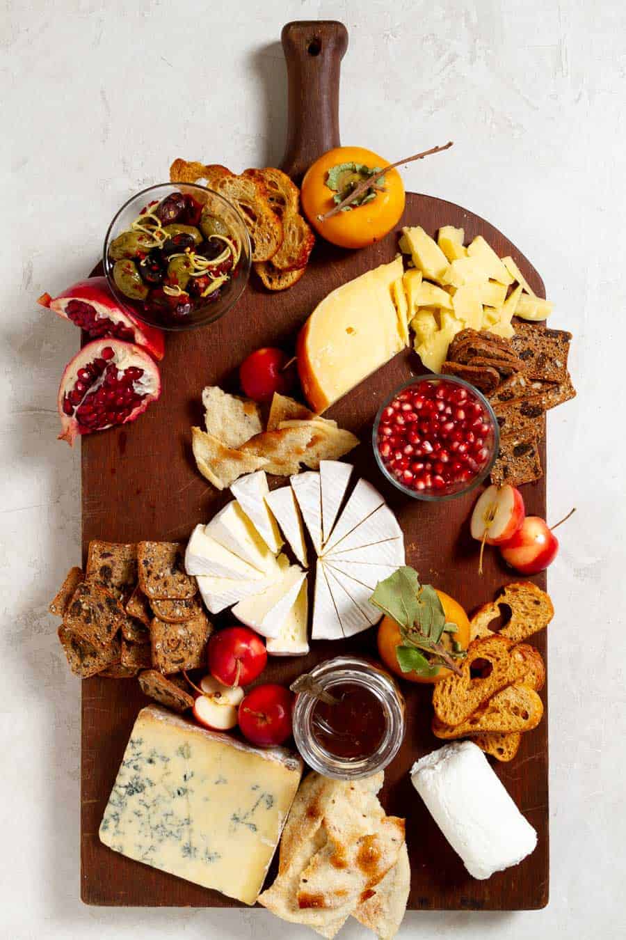 placing crackers on a wood board filled with cheeses and fruit.