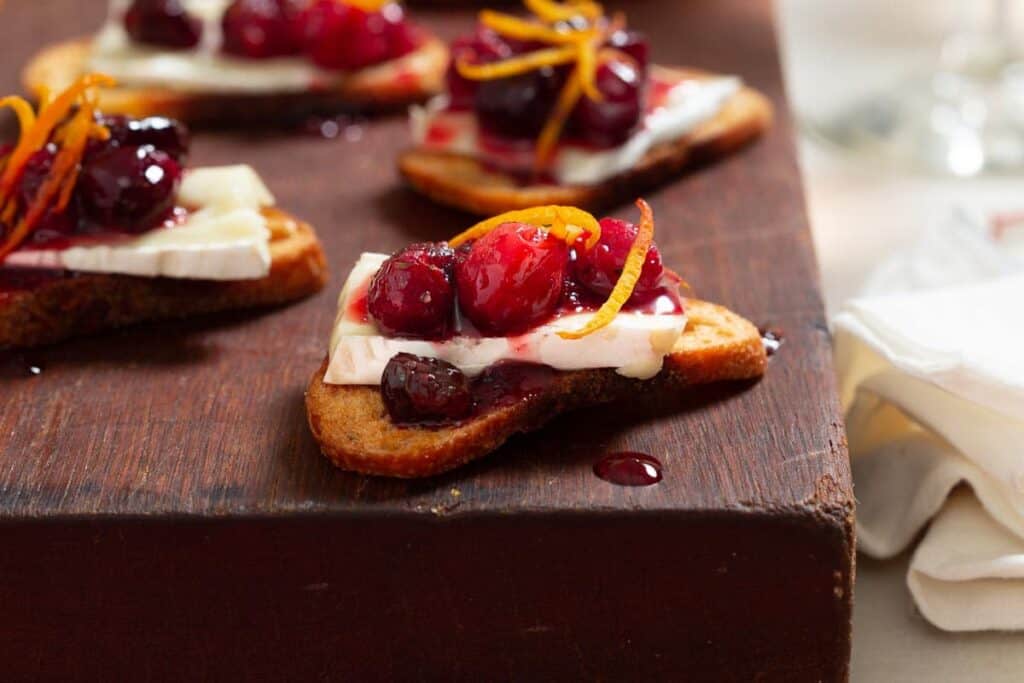 close up of a piece of crostini topped with a slice of brie, cranberry sauce and orange zest