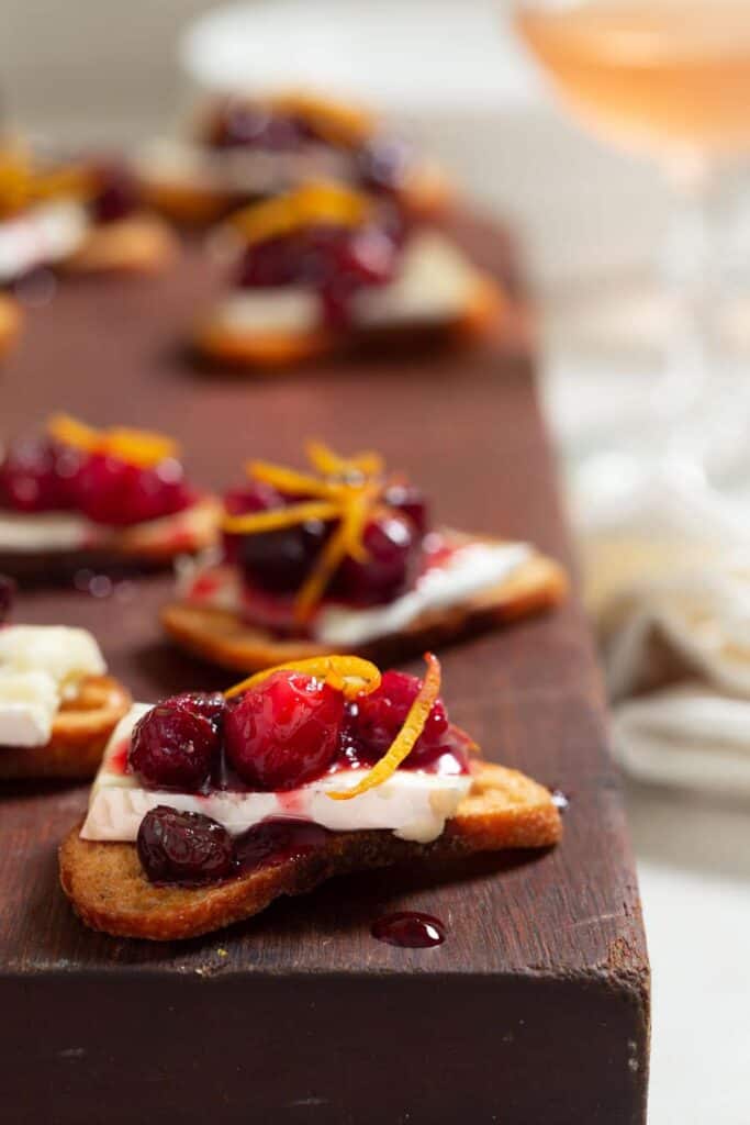 large dark wood cutting board topped with crostini topped with brie and cranberry sauce.