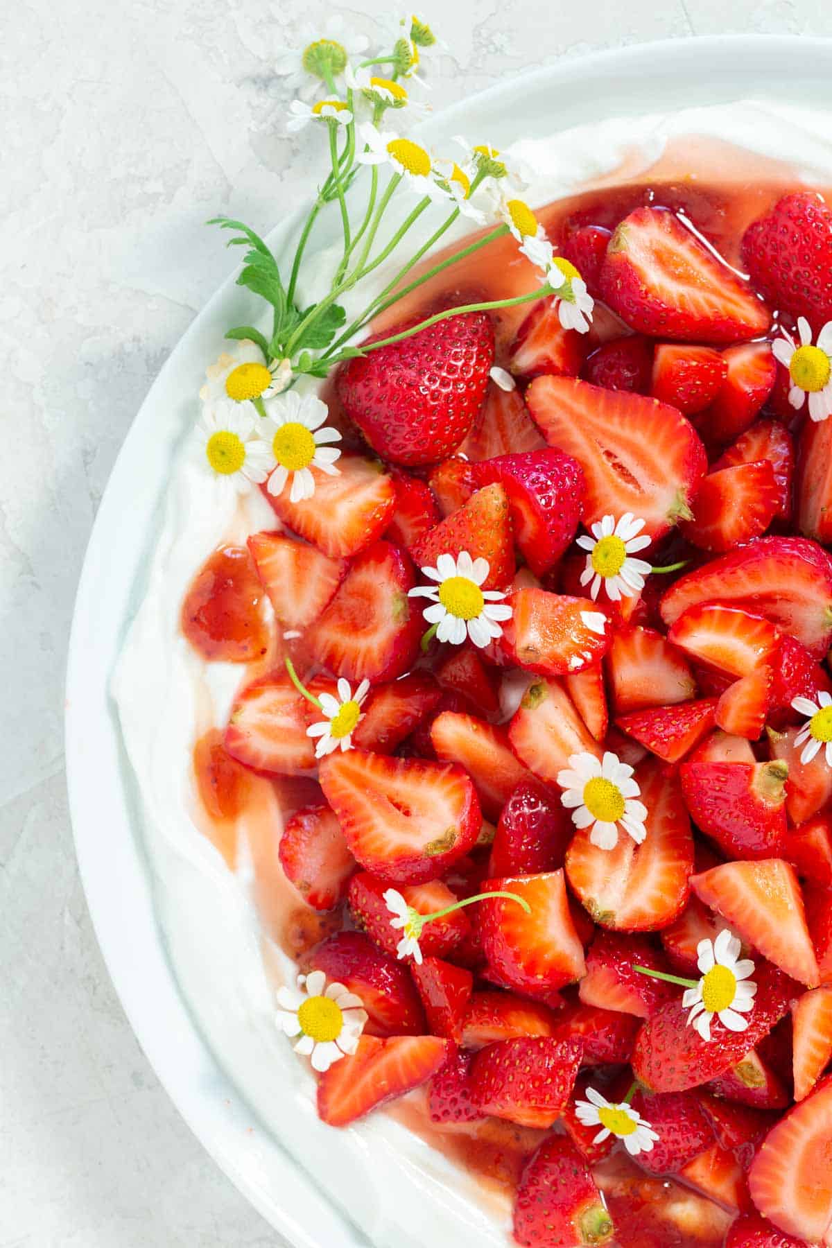 Close up of strawberry fruit salad with chamomile syrup on a white platter and garnished with fresh chamomile flowers.