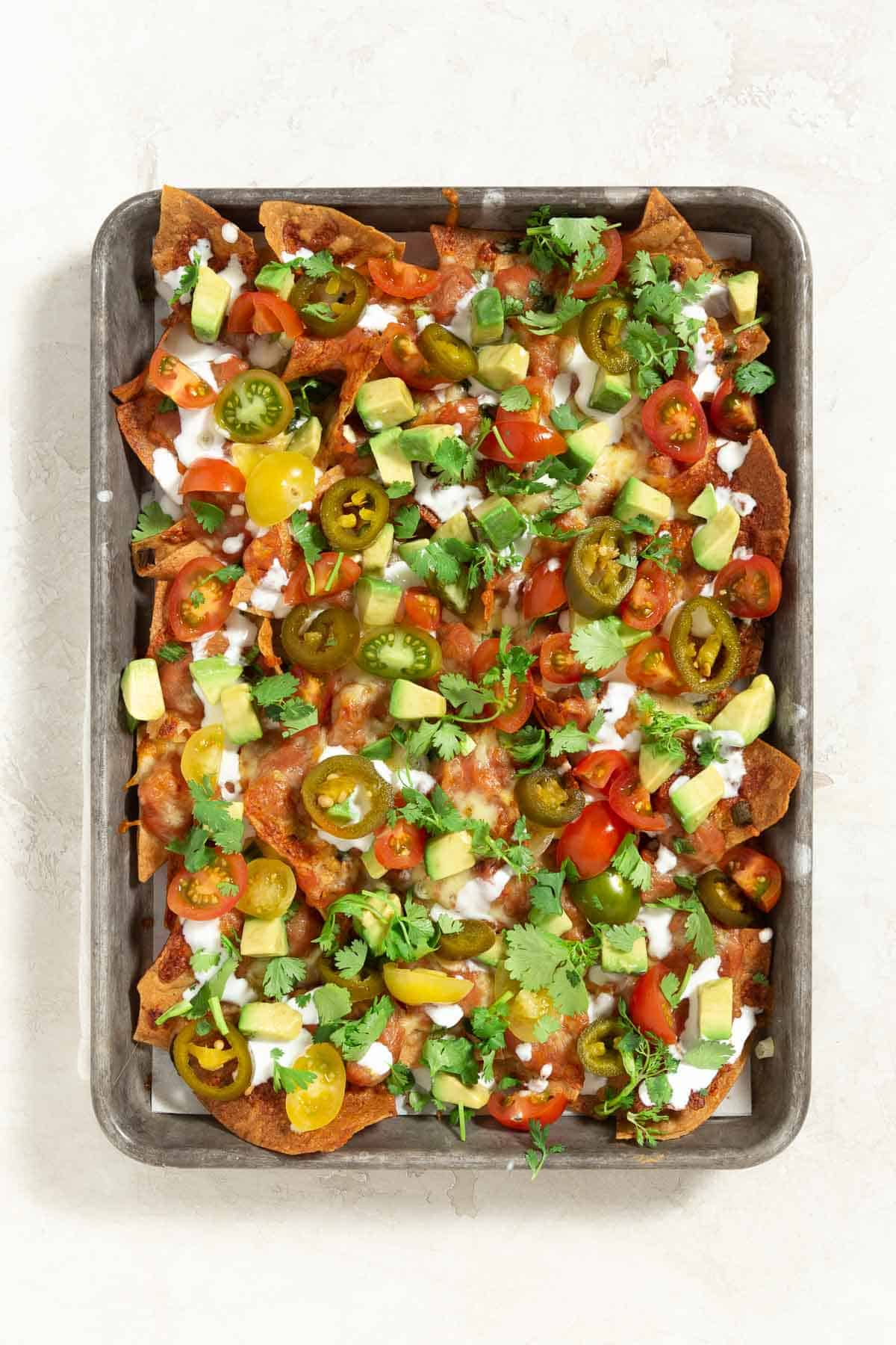 sheet pan with nachos layered with vegetables and cheese on top