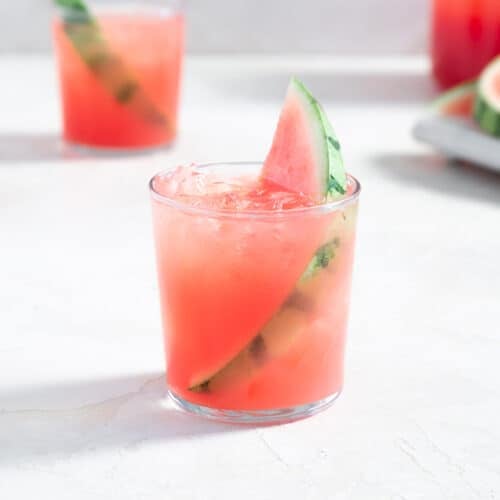 glass filled with a pink beverage, ice, and a slice of watermelon