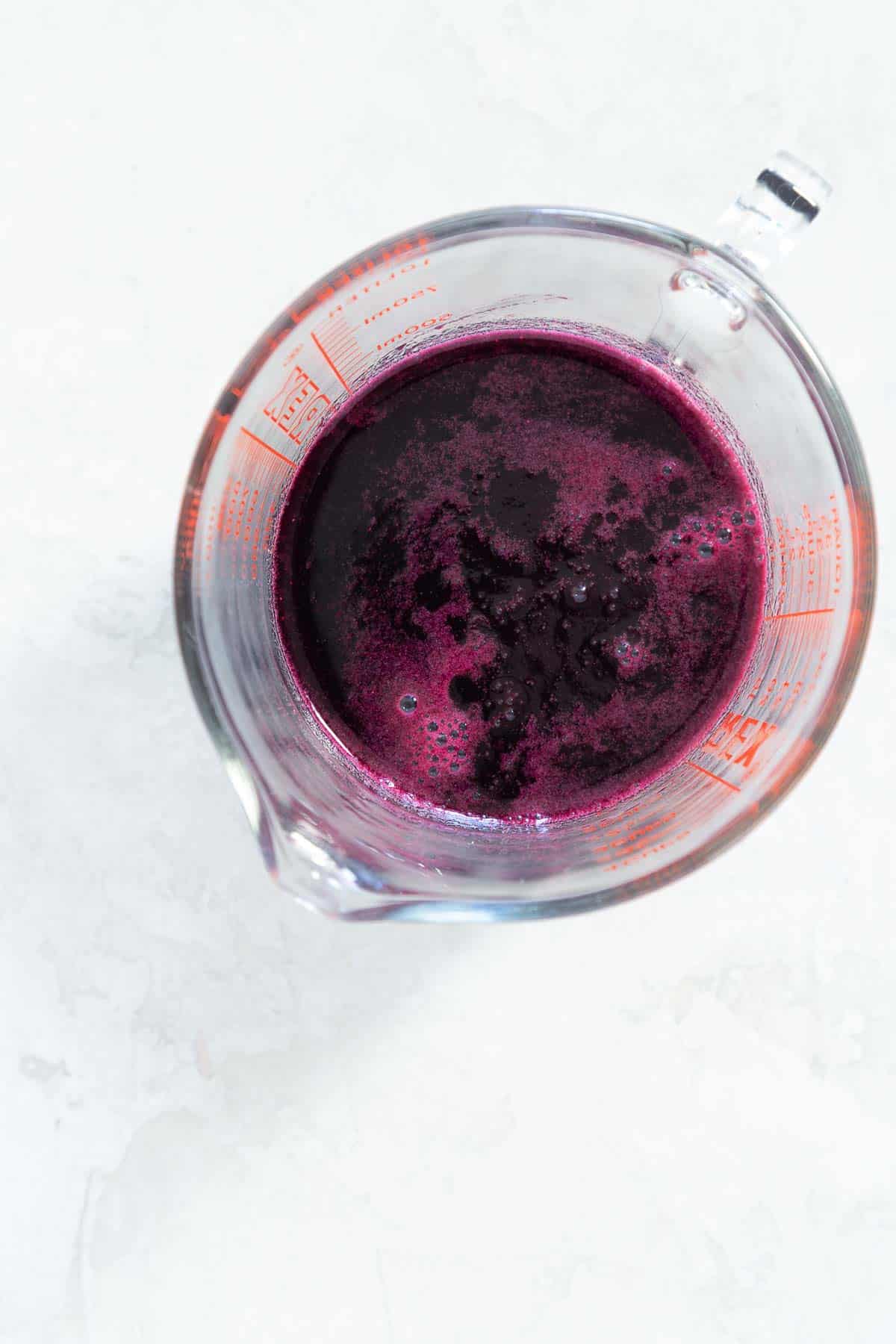 Overhead view of a measuring cup with purple blueberry syrup