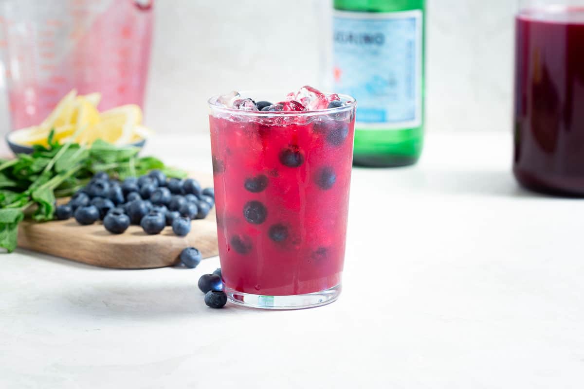 Glass of red lemonade with blueberries and ice.
