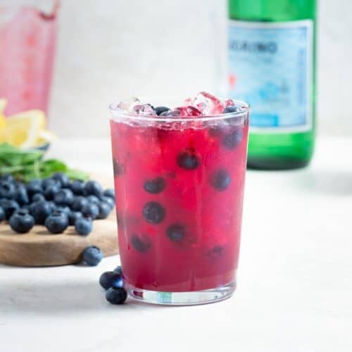 Close up of a glass of blueberry lemonade with fresh blueberries and ice