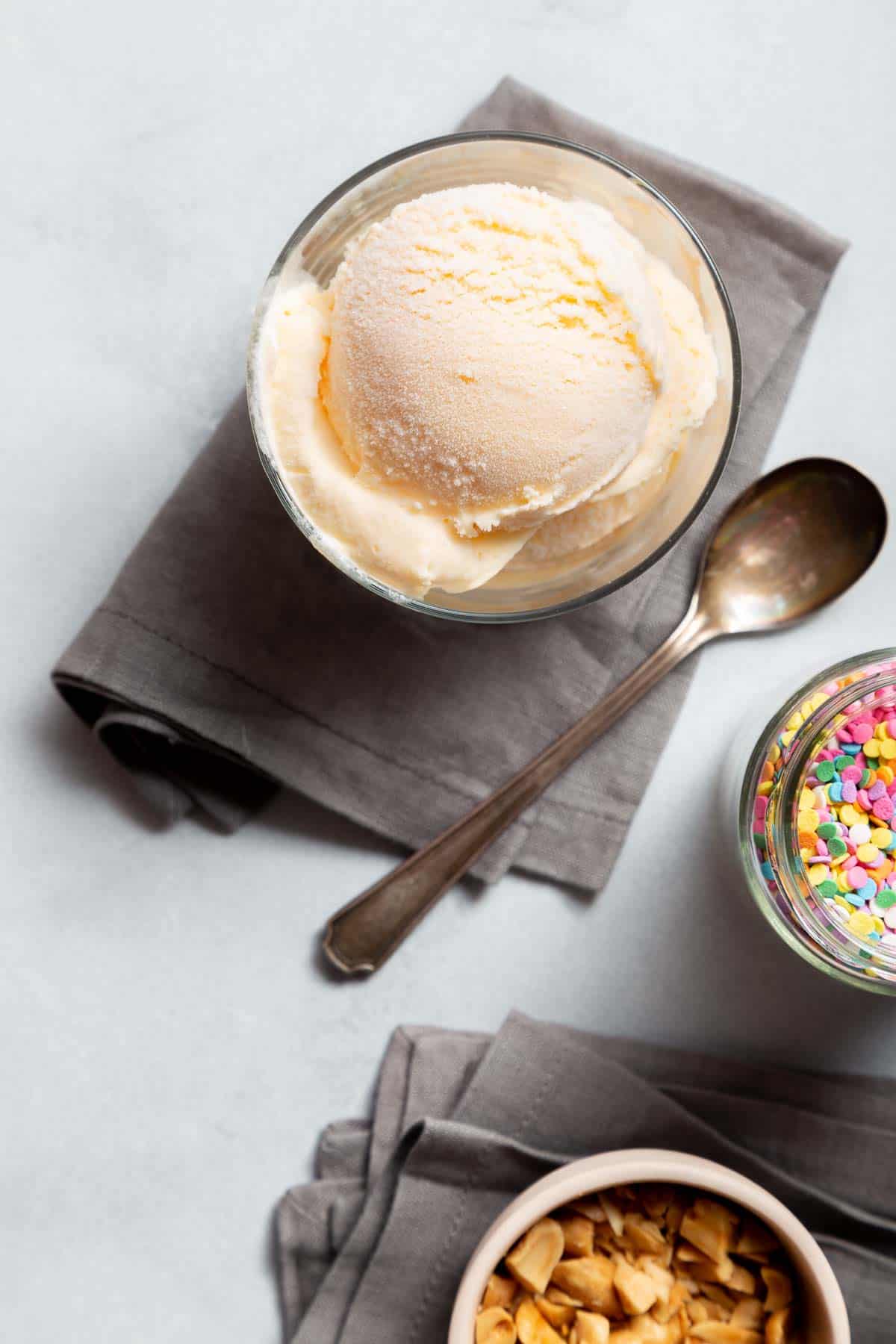 overhead view of a scoop of white ice cream in a white cup with a spoon on the side