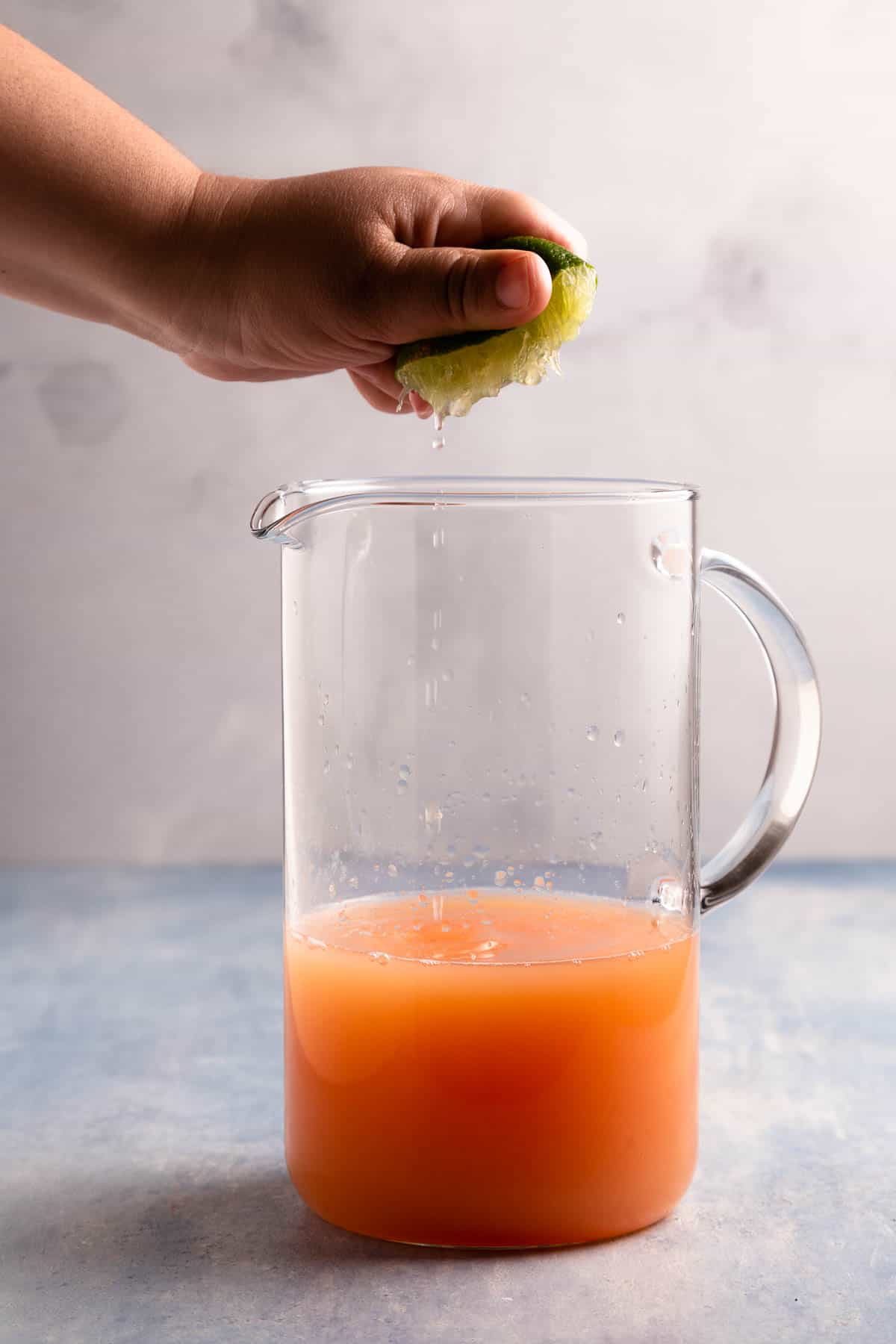 Woman's hand squeezing a lime into a pitcher filled with orange liquid