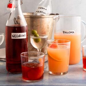 Closeup of glasses filled with cocktails and large bottles and pitchers in the background