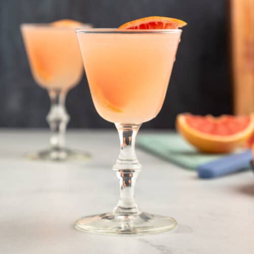 pink cocktail in a stemmed glass garnished with a slice of grapefruit