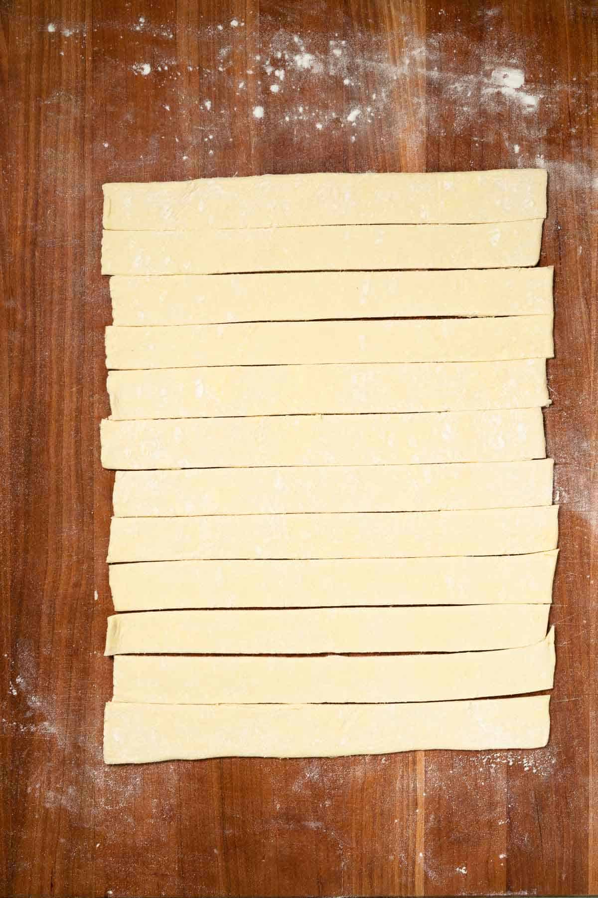 slicing a sheet of puff pastry on a cutting board