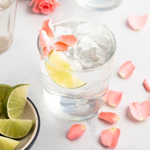 gin and tonic in a rocks glass with flower petals and lime