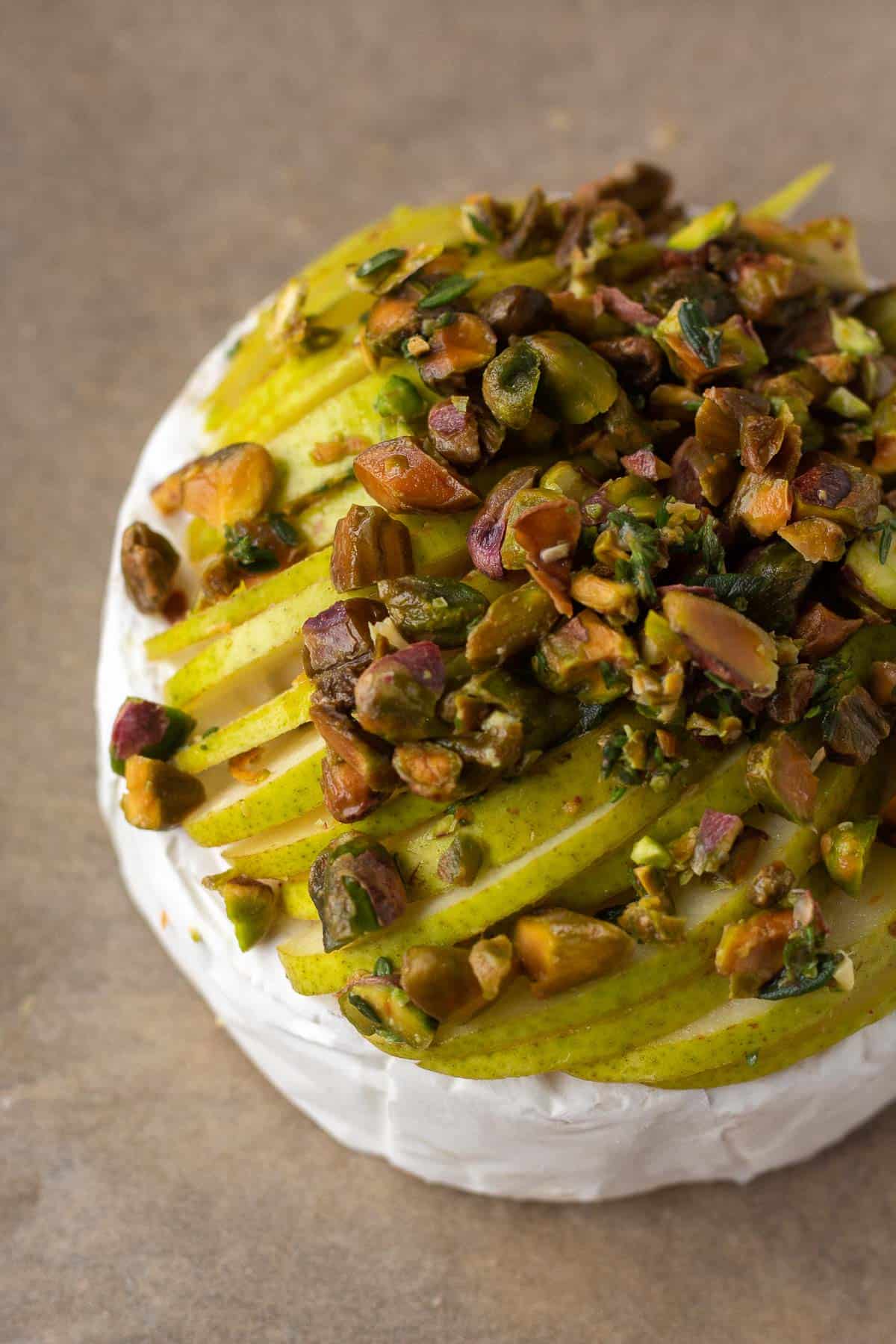 overhead of a wheel of brie topped with sliced green pears and toasted pistachios