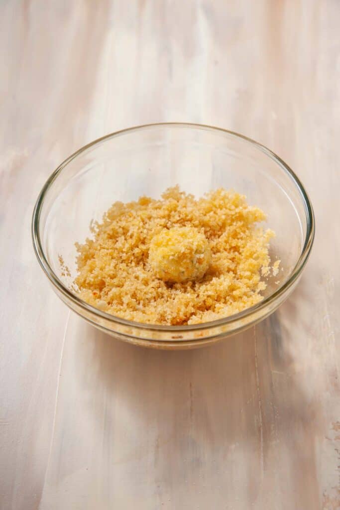 raw goat cheese ball being coated in a panko mixture