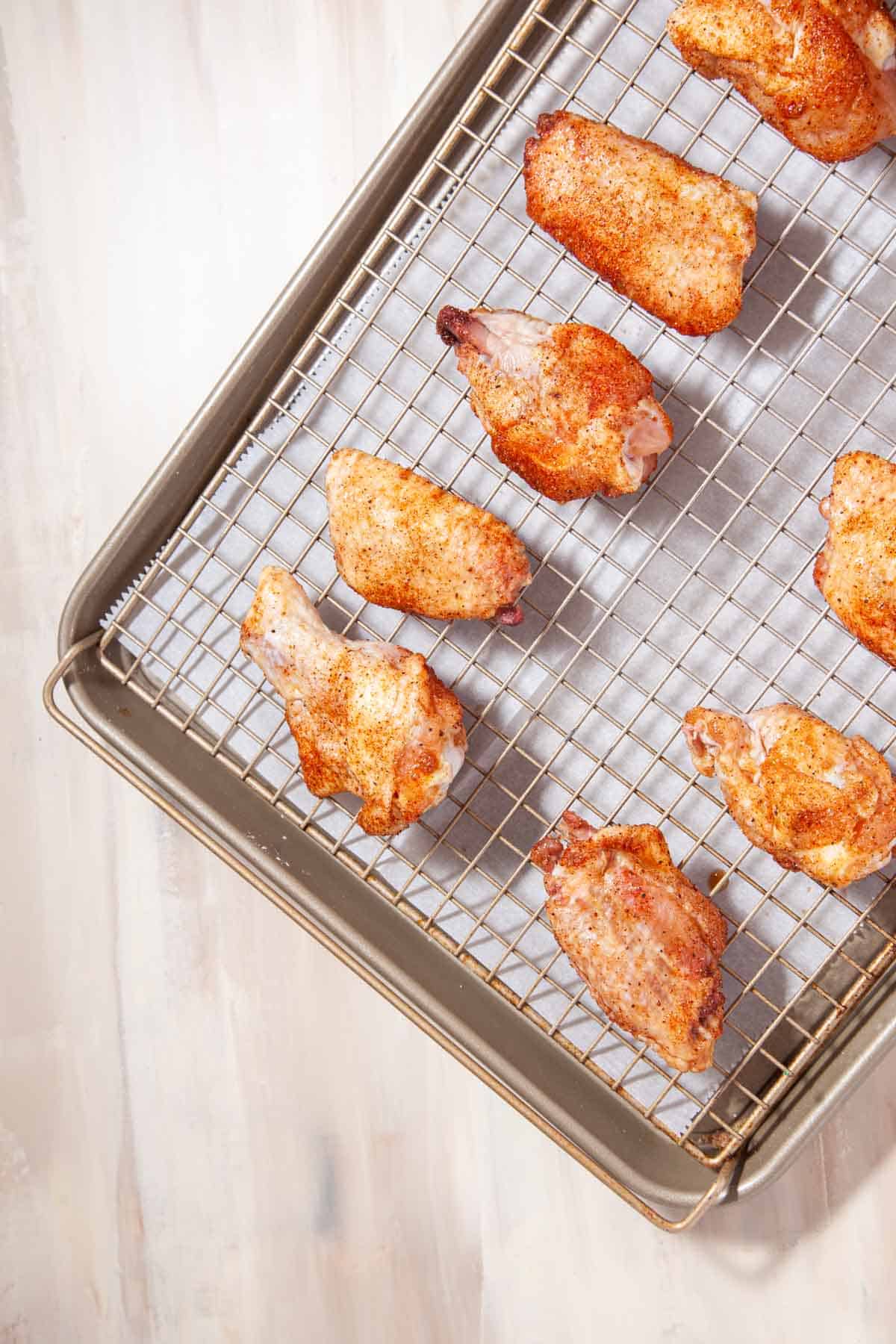 raw chicken wings coated in spices in rows on a wire rack.