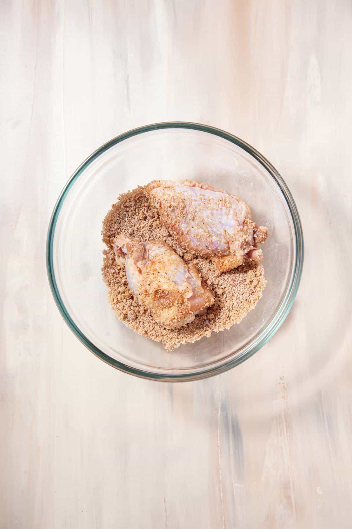 tossing raw chicken wings in a beige spice blend.
