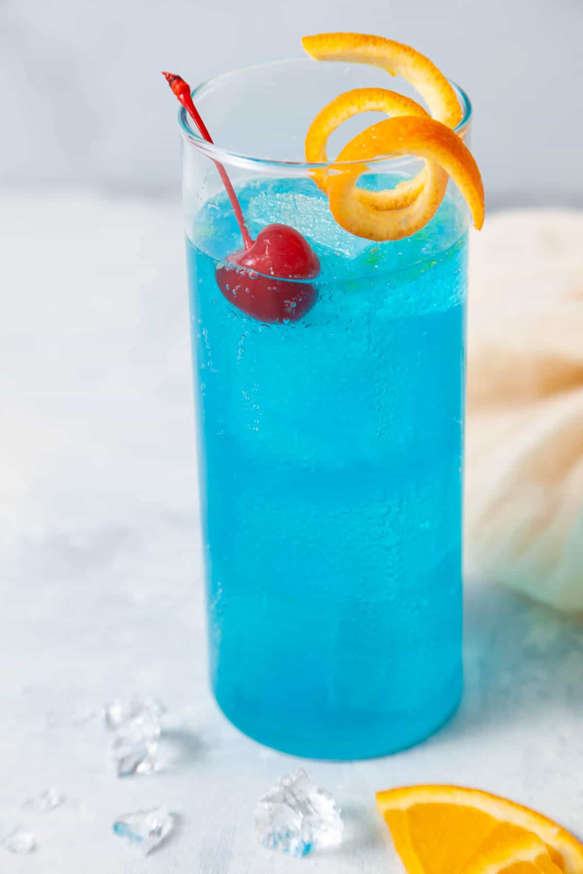 blue lagoon mocktail garnished with an orange peel and a cherry.