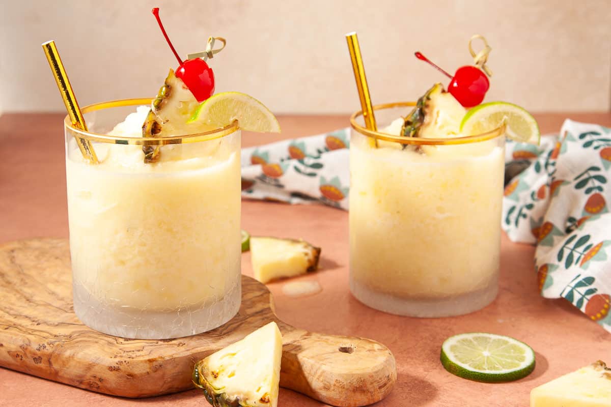 2 pina colada mocktails in glasses garnishes with pineapple, lime, and a cherry.