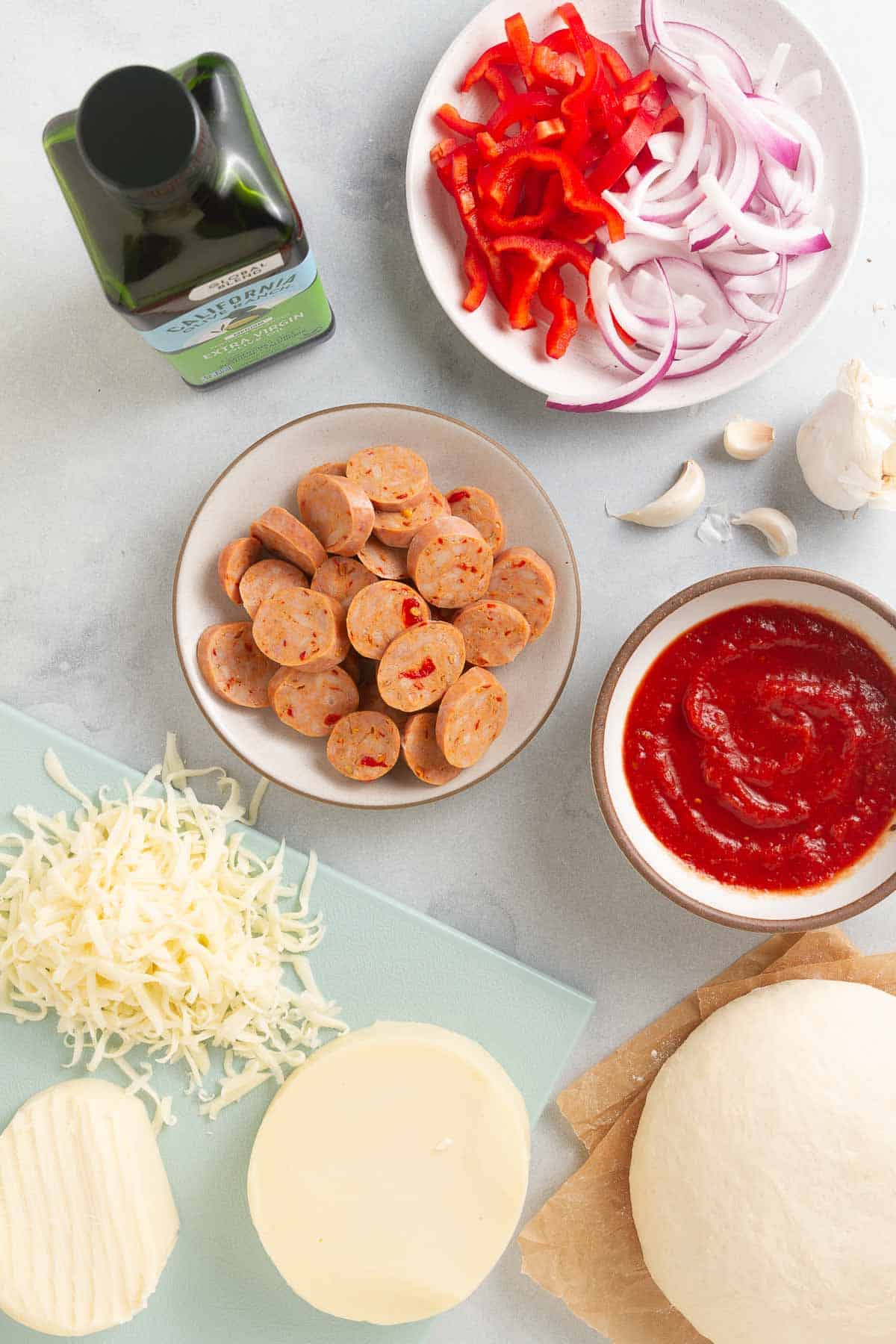 Ingredients for chicken sausage pizza in small white bowls.