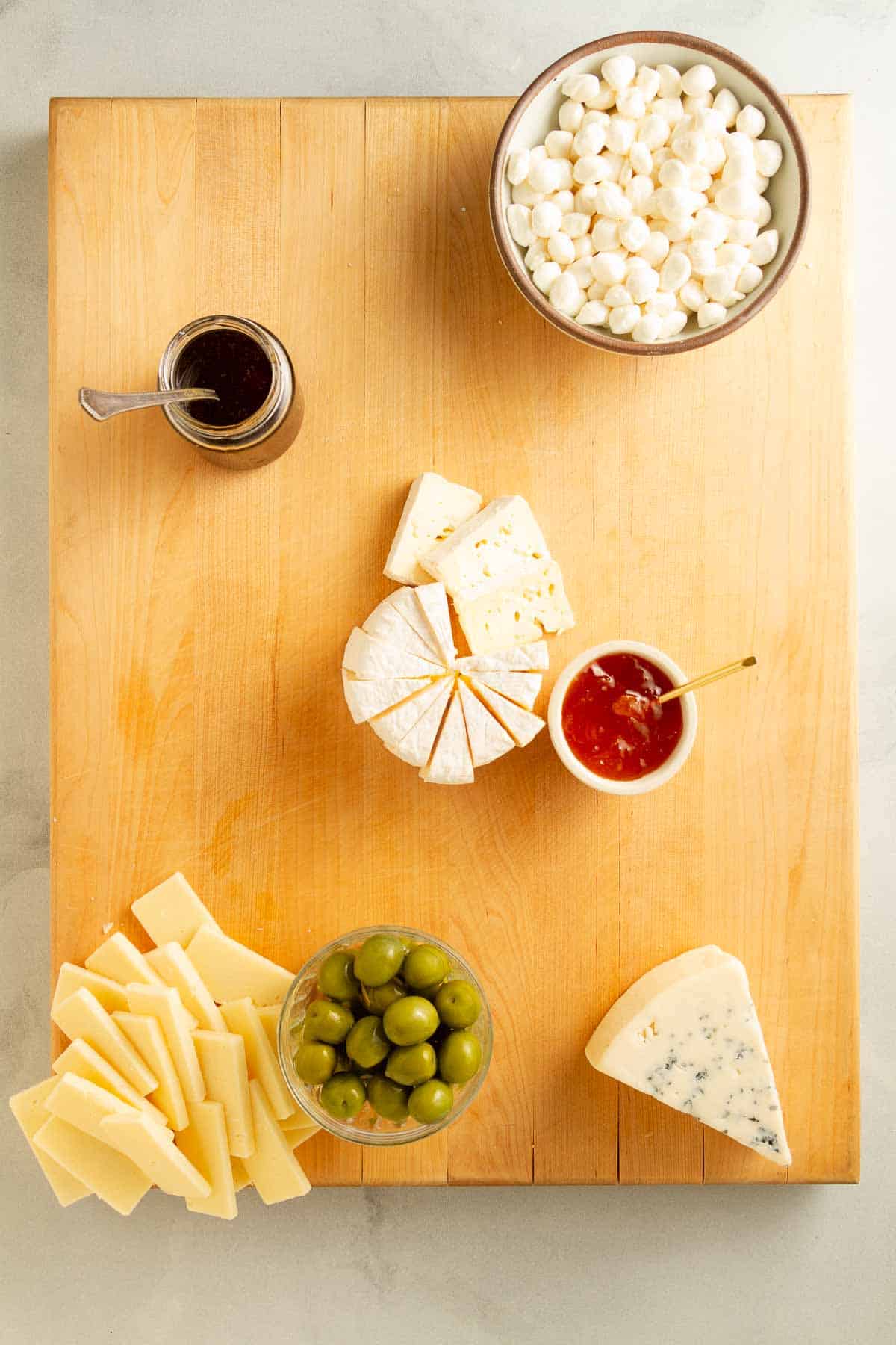 different types of cheeses and preserves on a wood board.