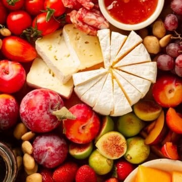 close up on fruit, cheese, and meat together on a board.
