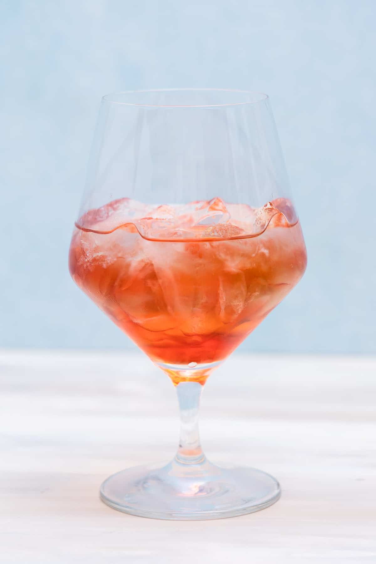 A large wine glass filled with an orange/pink beverage and ice.