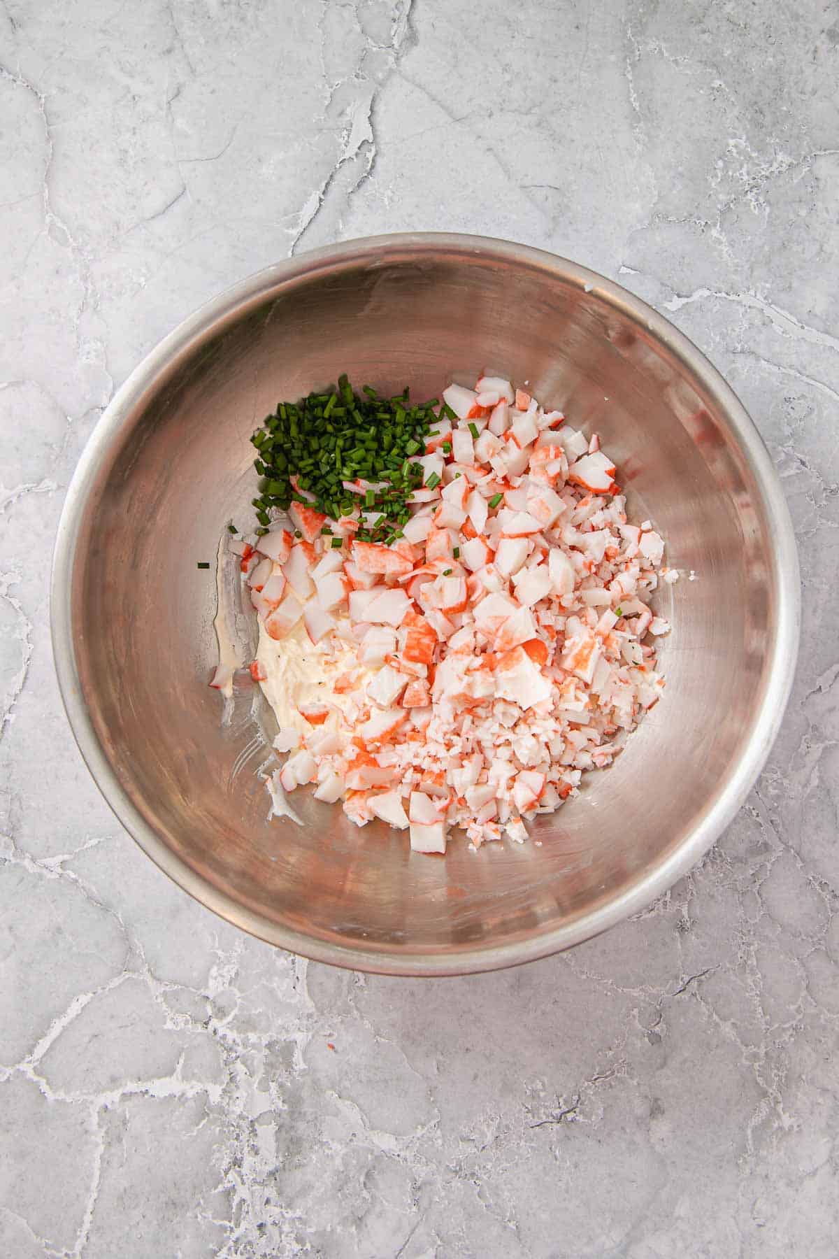 A metal bowl with chopped imitation crab meat and chives on top of a creamy mixture.