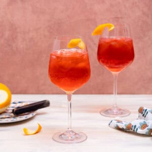 Two wine glasses filled with ice and a bright red liquid in them, and garnished with an orange twist.