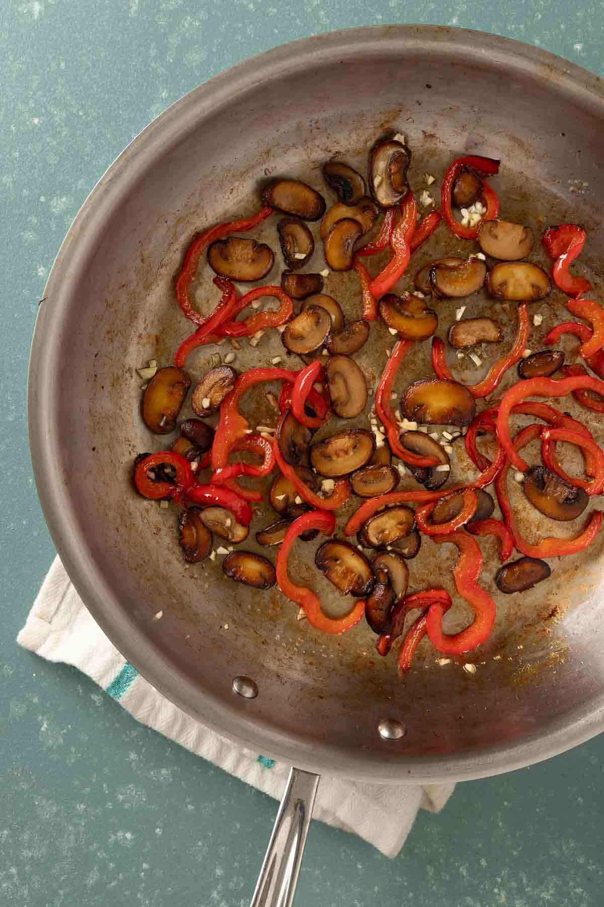 Overhead of a stainless steel pan with cooked mushrooms, bell peppers and garlic in it.