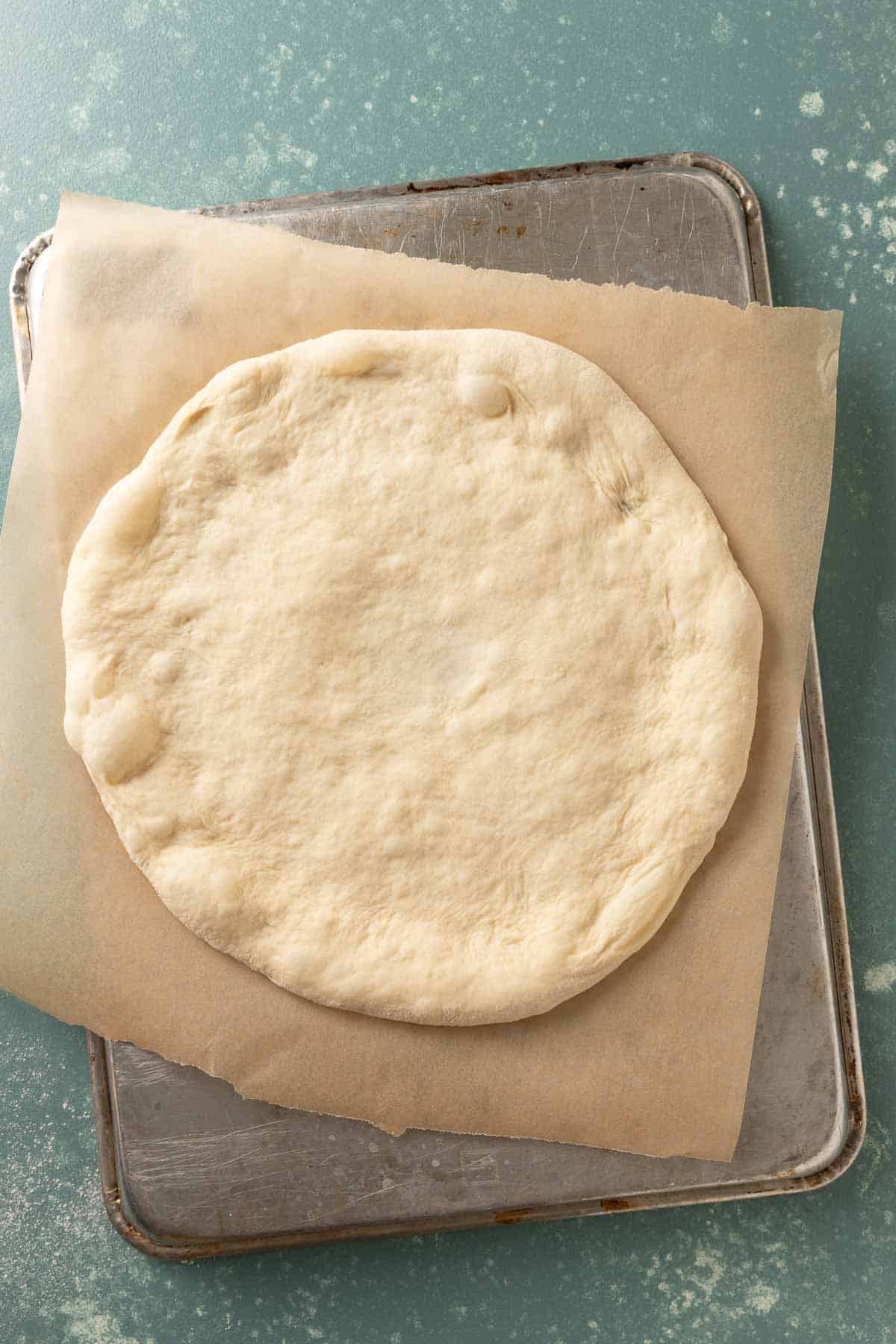 Overhead of pizza dough stretched out on a piece of brown parchment paper.