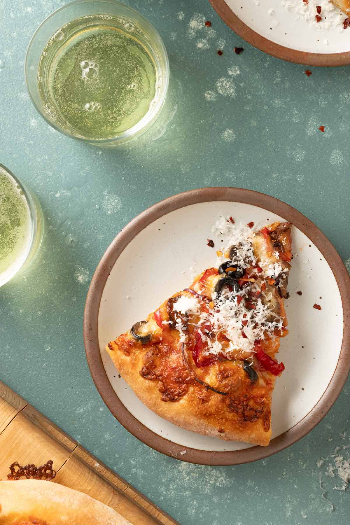Overhead of a slice of pizza on a small plate with a glass of cider next to it.