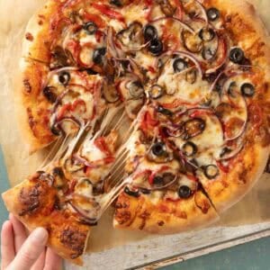 Overhead of a whole pizza with a slice being taken out of it.