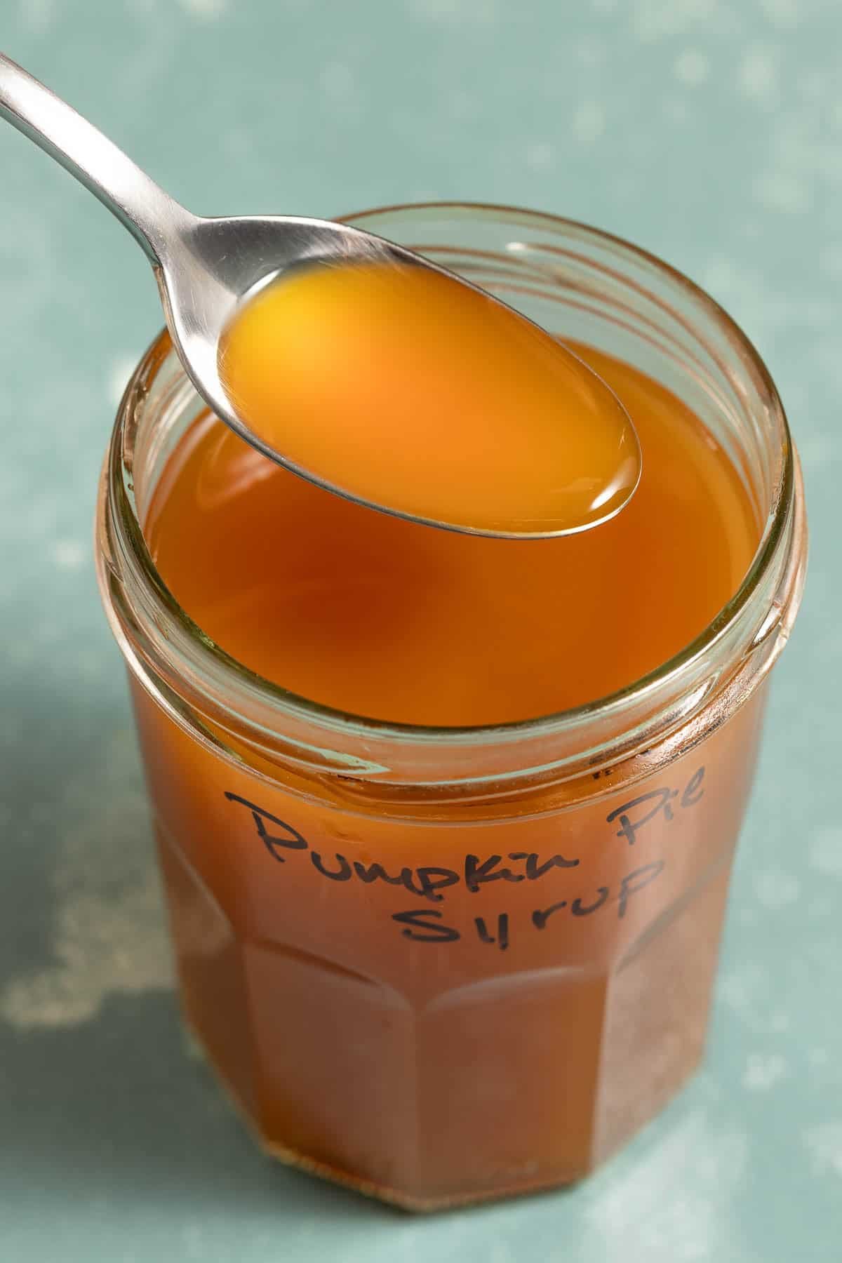 An orange liquid on a spoon over a jar of the same liquid.