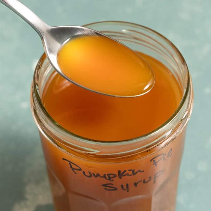 An orange liquid on a spoon over a jar of the same liquid.