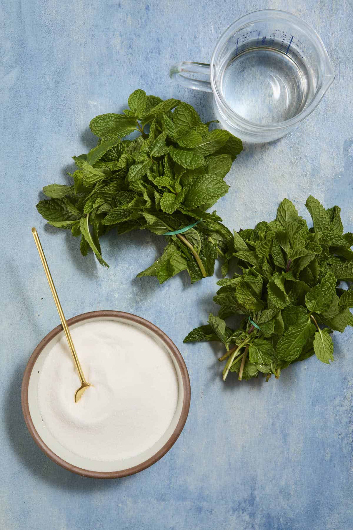 Two bunches of fresh mint next to a bowl of white sugar.