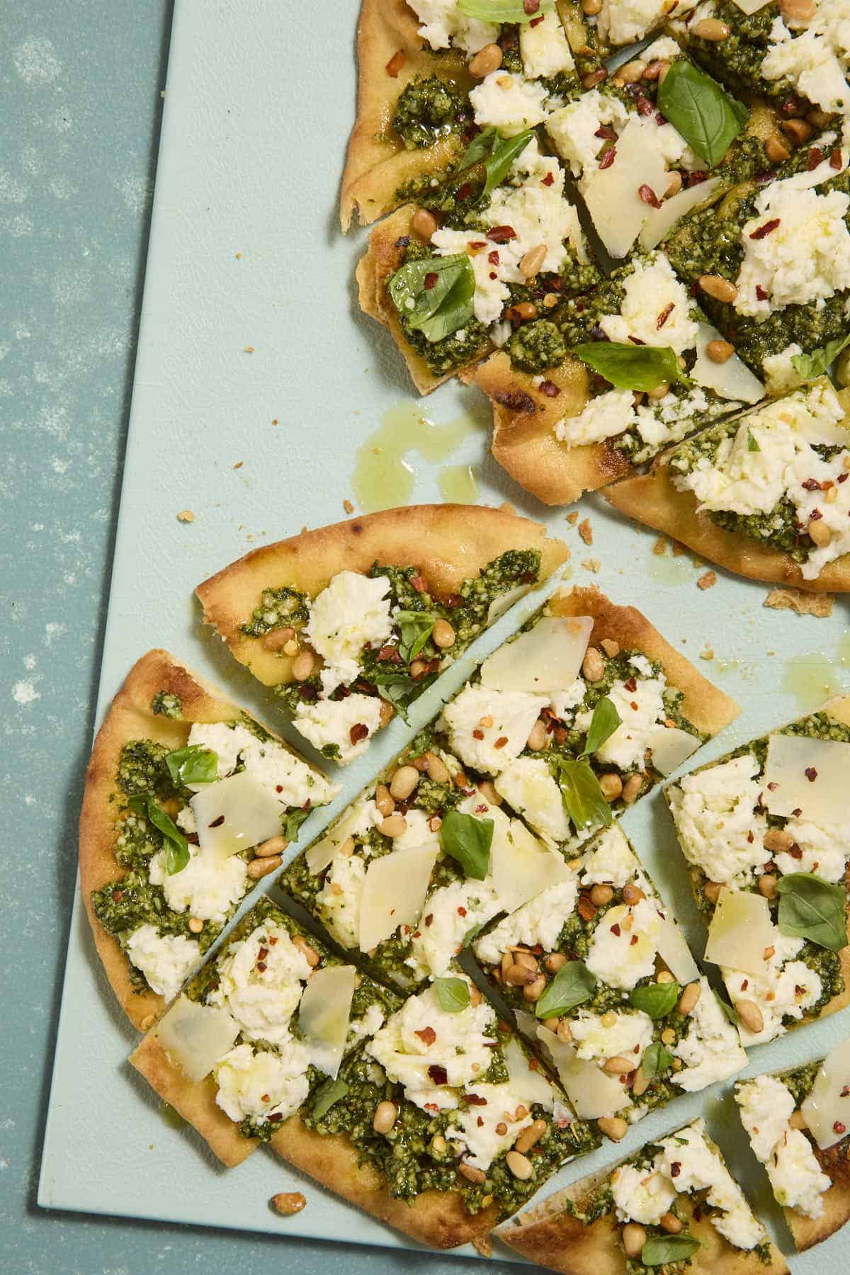 Pesto and mozzarella flatbread sliced into several small pieces on a blue cutting board.